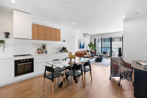 A modern kitchen with white cabinets, a built-in oven, and a dining area with a glass table and chairs.