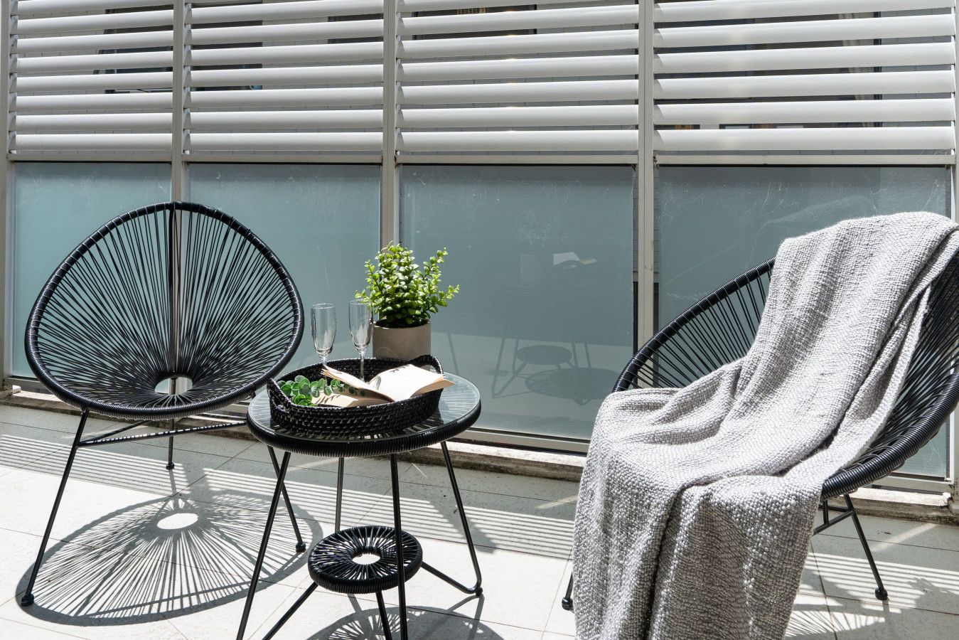A balcony with two black chairs, a small table with a plant and a book, and a glass of water.