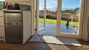 A kitchen with a refrigerator, microwave, and toaster, and a sliding glass door leading to a deck with a view of mountains. - Toradh Cabin (Spean Bridge)