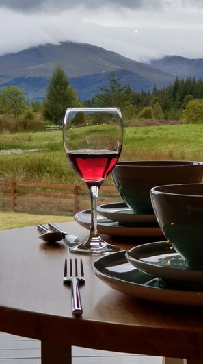 A table with a wine glass, cutlery, and bowls set outdoors with a mountainous landscape in the background. - Toradh Cabin (Spean Bridge)
