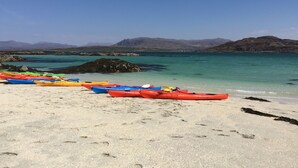 A beach with kayaks lined up on the sand and a clear view of the sea and mountains in the background. - Toradh Cabin (Spean Bridge)