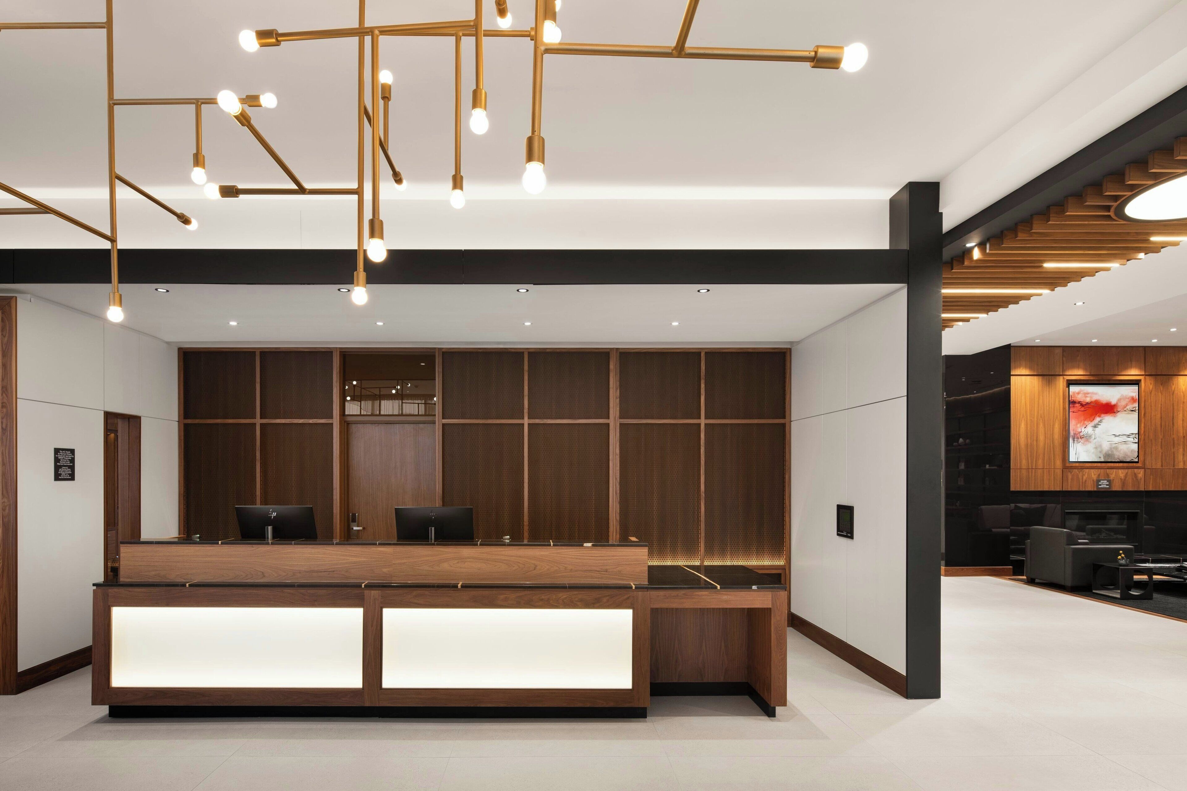 A modern reception area with a wooden reception desk, a seating area with sofas, and a large TV screen.