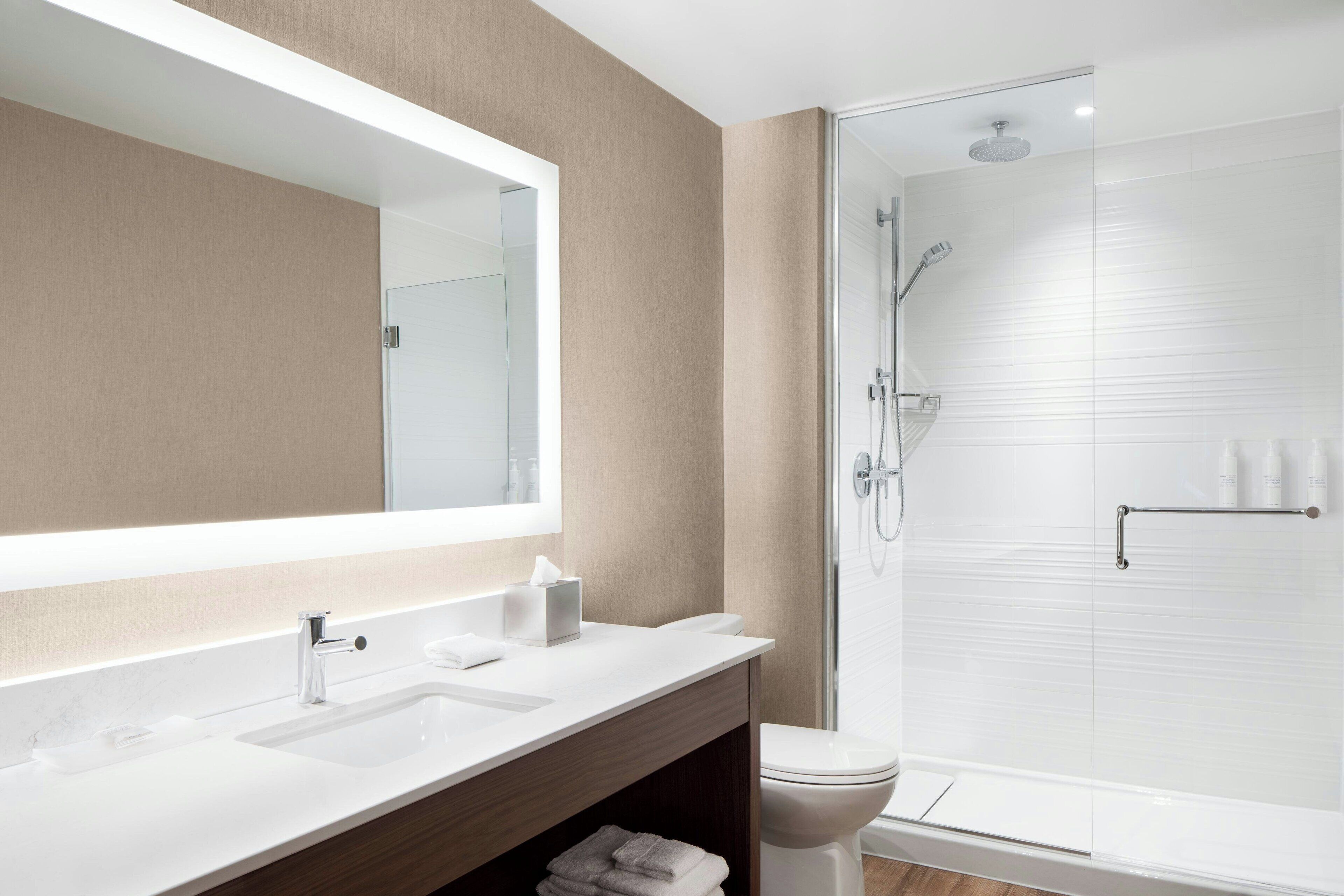 A modern bathroom with a large mirror, two sinks, a toilet, and a glass-enclosed shower.