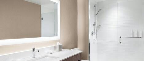 A modern bathroom with a large mirror, two sinks, a toilet, and a glass-enclosed shower.