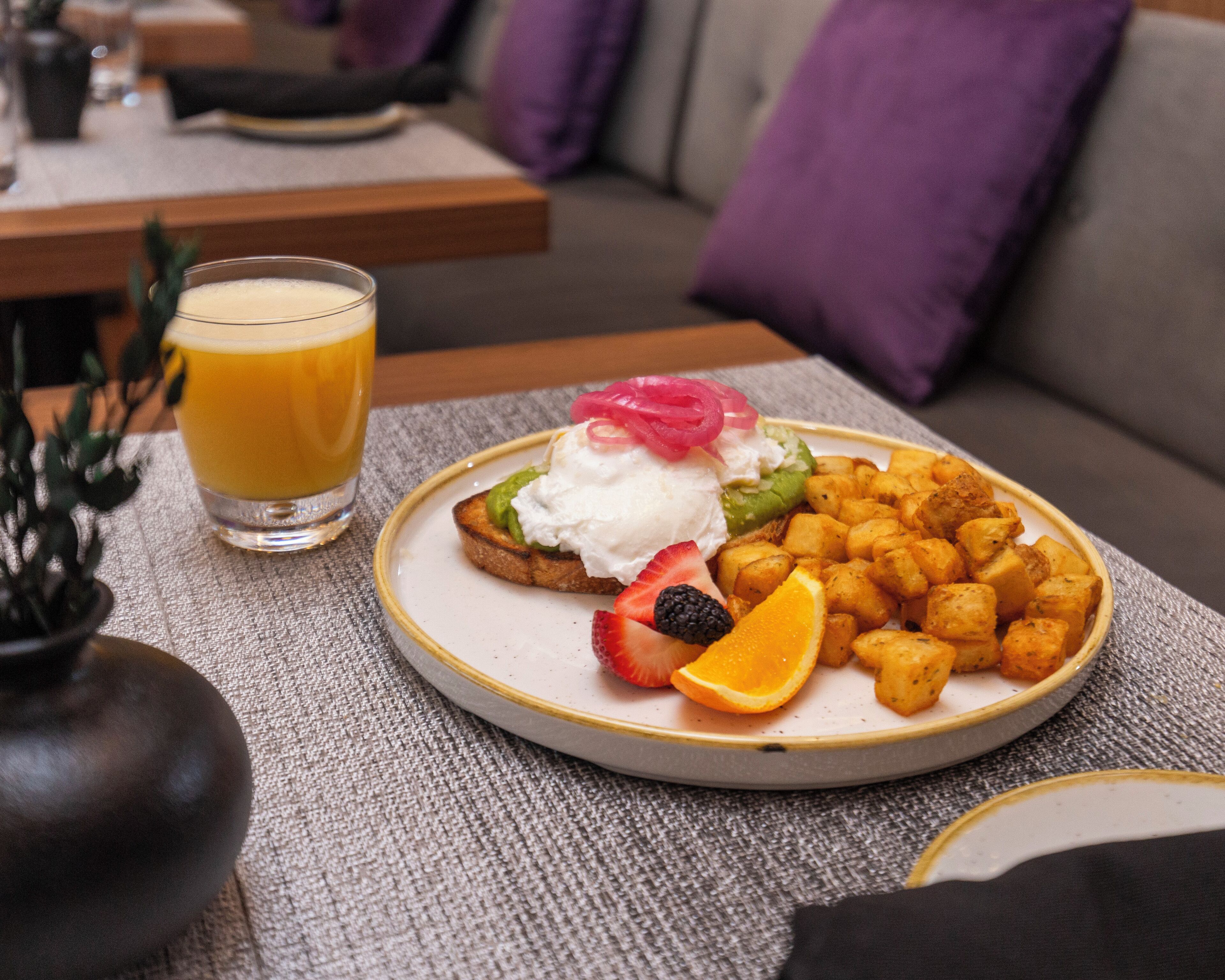 A plate of food with toast, fruit, and potatoes, and a glass of orange juice on a table.