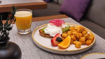 A plate of food with toast, fruit, and potatoes, and a glass of orange juice on a table.