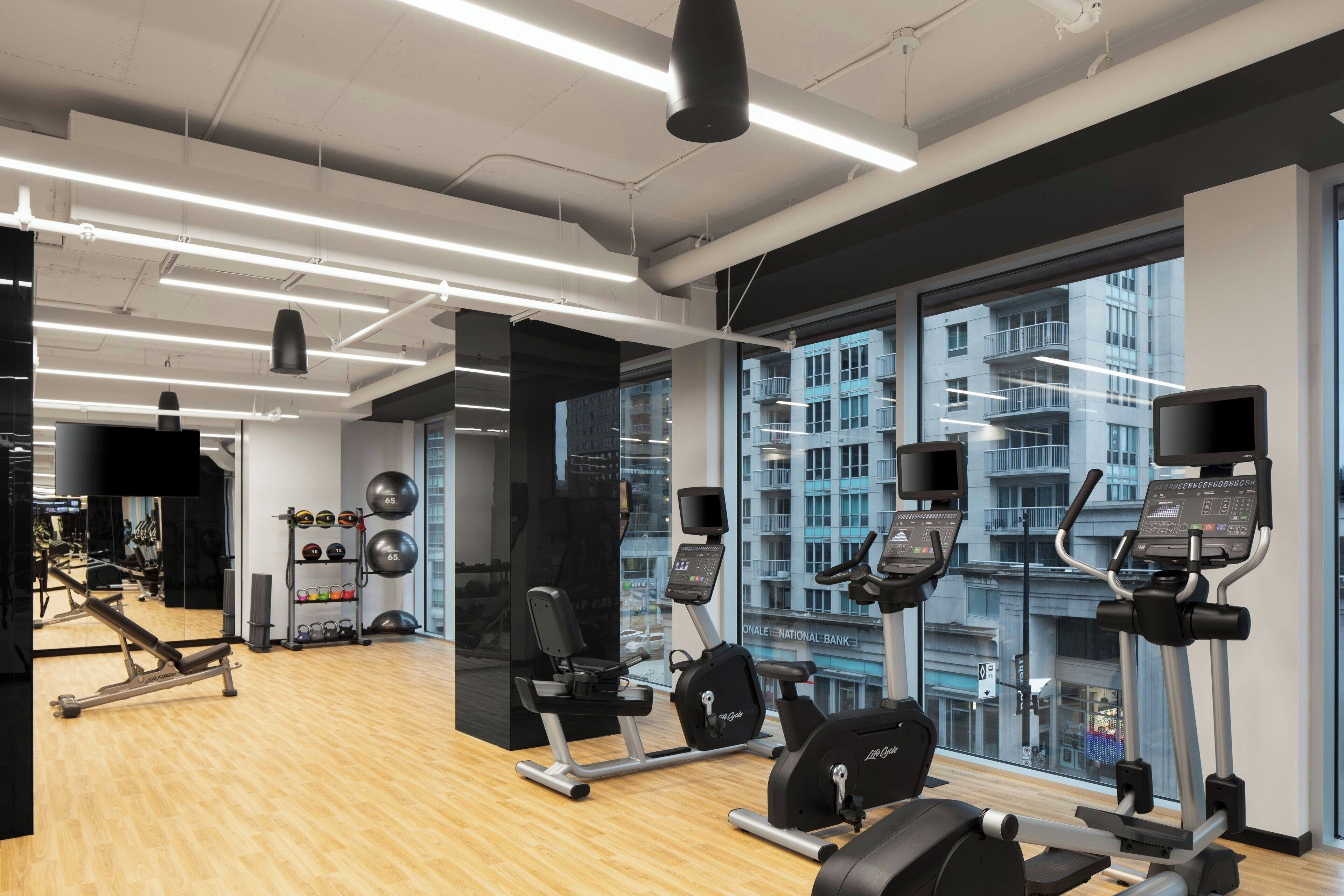Ett modernt gym med träningsutrustning, stora fönster och utsikt över staden.