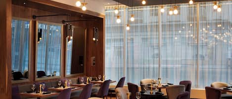 A modern restaurant with wooden walls, large windows, and pendant lighting.