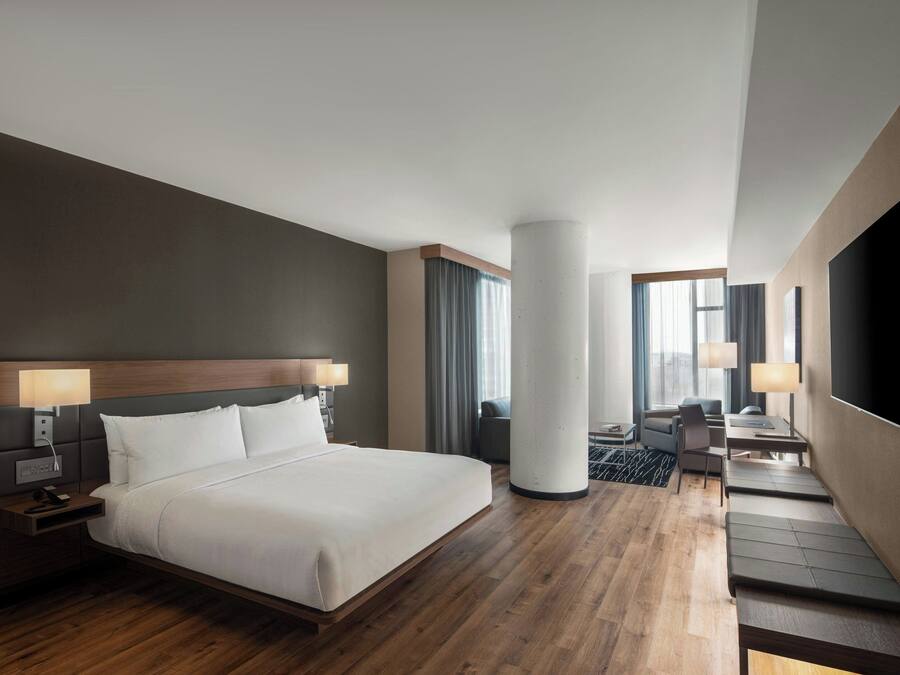 Ein modernes Hotelzimmer mit einem großen Bett, Nachttischen, einem Schreibtisch und einem Fernseher.