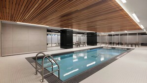 A modern indoor swimming pool with a wooden ceiling, tiled floor, and black lounge chairs. - AC Hotel BY Marriott Ottawa Dwtn (OTTAWA)