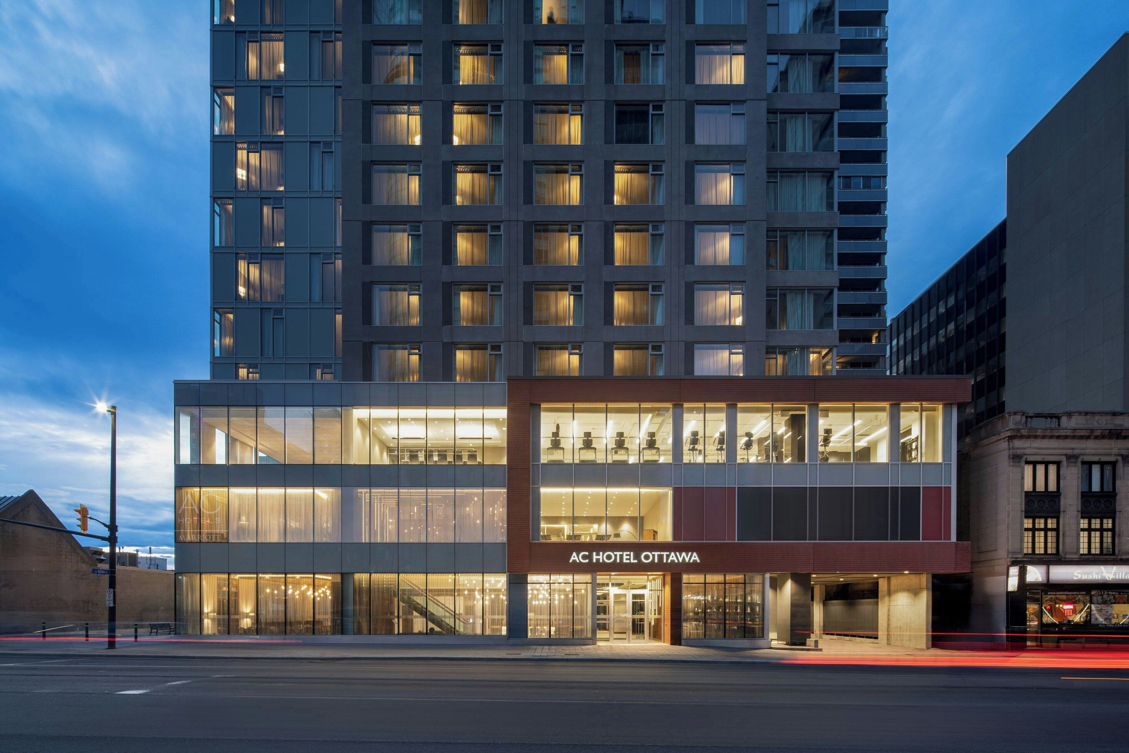 A modern hotel with a glass facade, a visible entrance, and a sign reading "AC HOTEL OTTAWA".