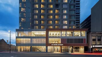 A modern hotel with a glass facade, a visible entrance, and a sign reading "AC HOTEL OTTAWA".