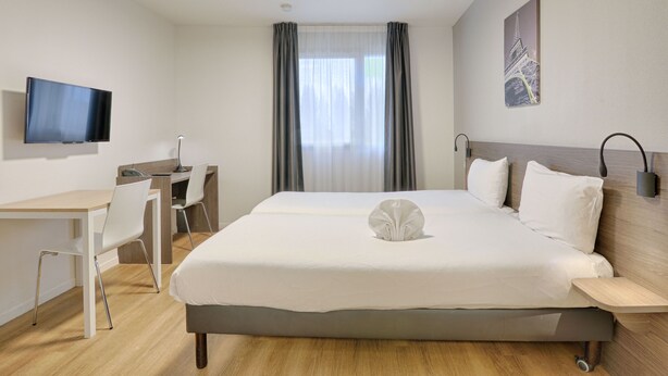 A hotel room with a bed, a desk, a chair, a flat-screen TV, and a window with curtains. - Cosy studio proche RER, idéal pour visiter Paris (Nogent-sur-Marne)