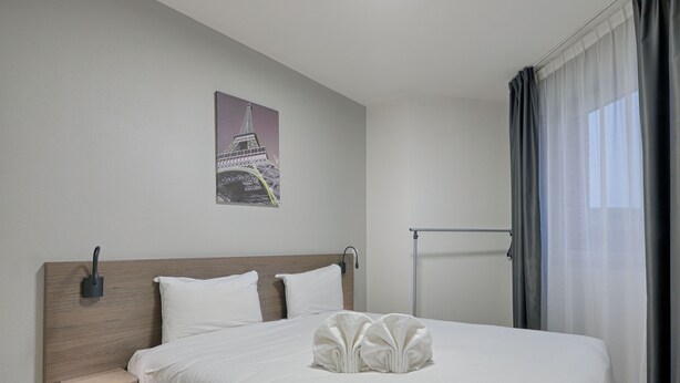 A neatly made bed with white linens, a wooden headboard, a small bedside table, and a wall-mounted lamp. - À 3 km de la gare RER E | Accès rapide à Paris (Nogent-sur-Marne)