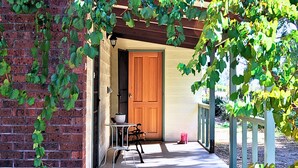 A brick building with a wooden door, a small table, and a chair outside. - UzuriBarossa, Tranquil guesthouse retreat in Lyndoch, Barossa Valley (Altona)