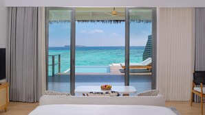 Een hotelkamer met een grote schuifglazen deur die leidt naar een balkon met zwembad en uitzicht op de oceaan.