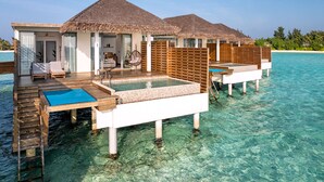 Bungalows op het water met rieten daken, houten terrassen en helderblauw water.