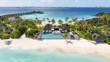 An aerial view of a resort with overwater bungalows, a swimming pool, and a beach.