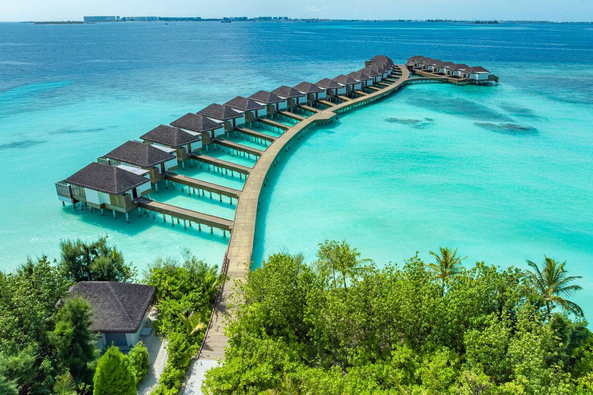 Un complexe hôtelier situé sur pilotis, composé de plusieurs hébergements de type bungalow reliés par une passerelle en bois.