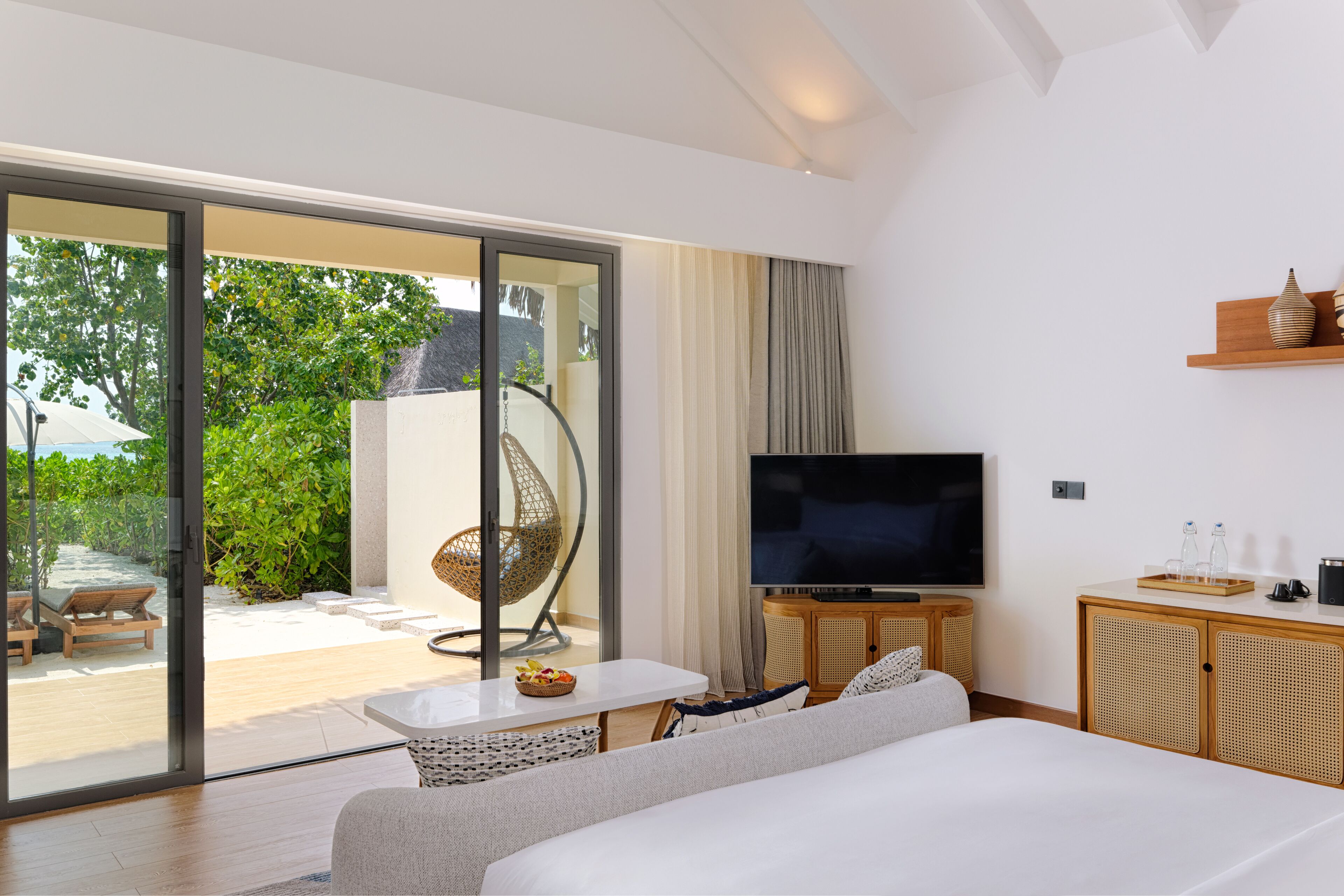Une chambre d’hôtel moderne dotée d’un grand lit, d’une télévision, d’une petite table et d’un balcon aménagé avec du mobilier d’extérieur.