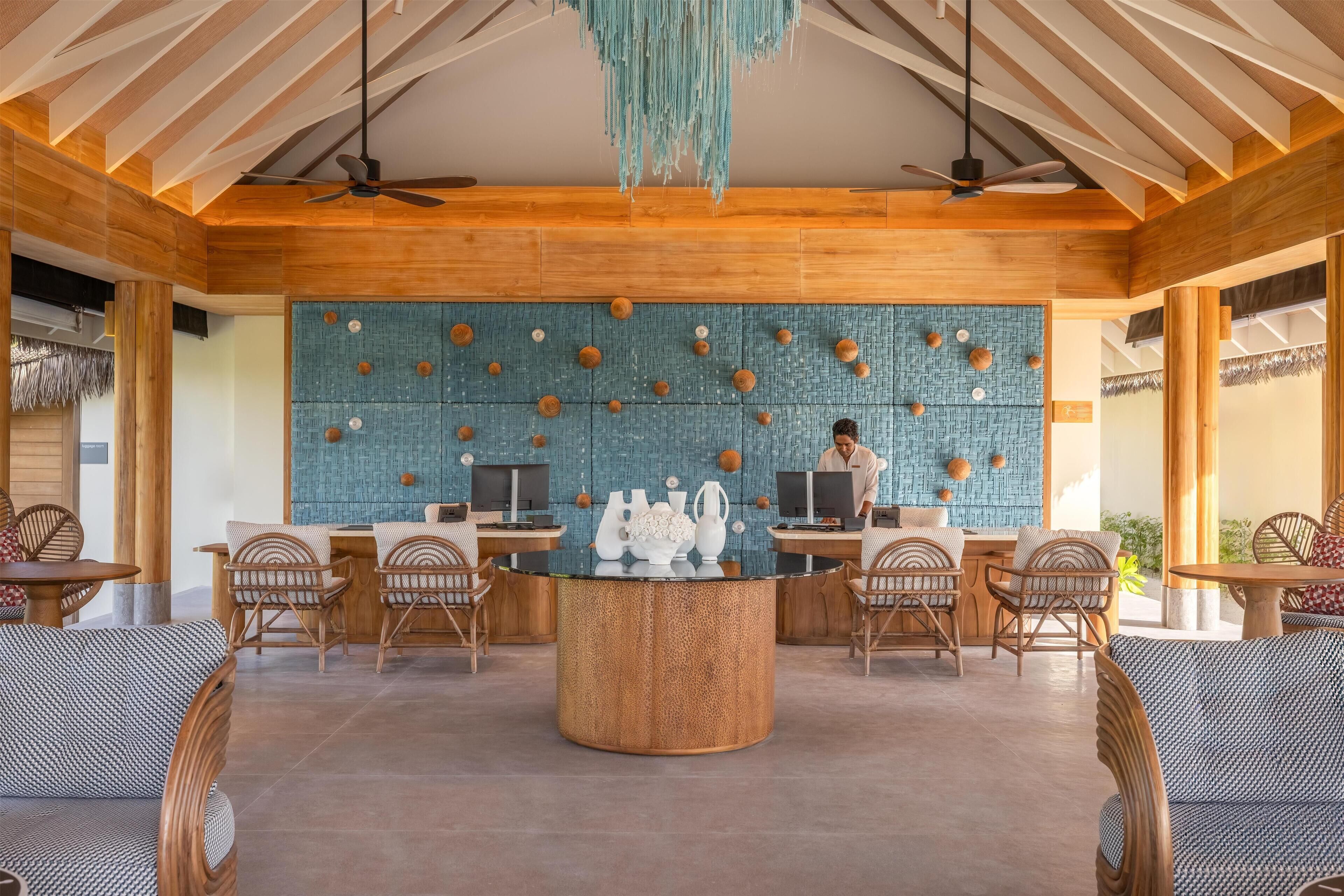 Un vestíbulo espacioso con vigas de madera, una mesa redonda central y una pared azul con textura y detalles decorativos.