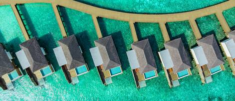 Vista aérea de un resort con una serie de bungalows sobre el agua, alineados a lo largo de un camino curvo.