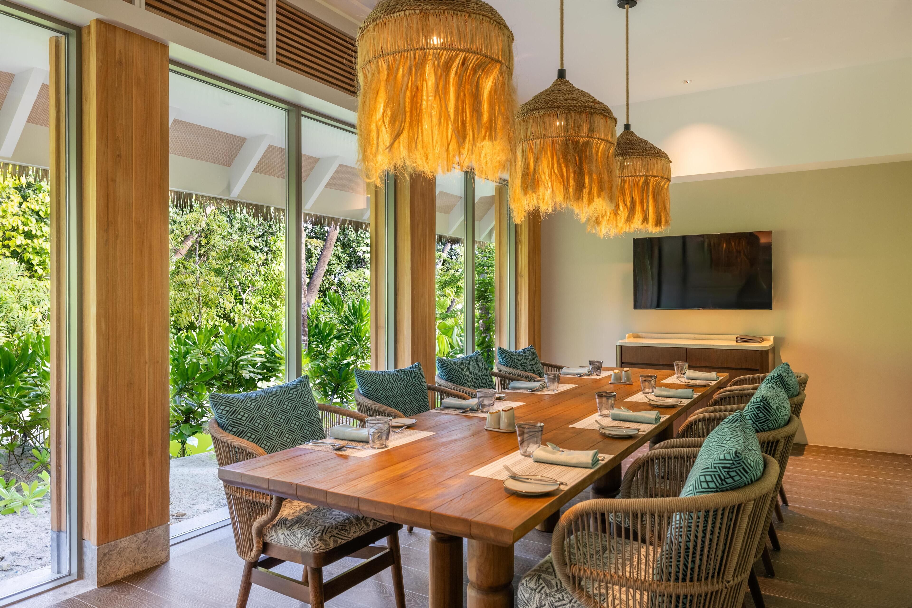 A dining area with a long wooden table, wicker chairs, and hanging lamps.