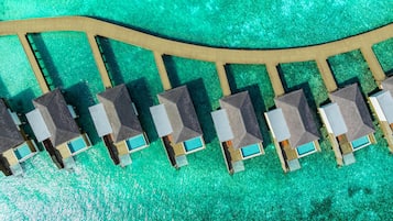 Vista aérea de un complejo turístico con bungalows sobre el agua, dispuestos en una formación curva a lo largo de una pasarela de madera.