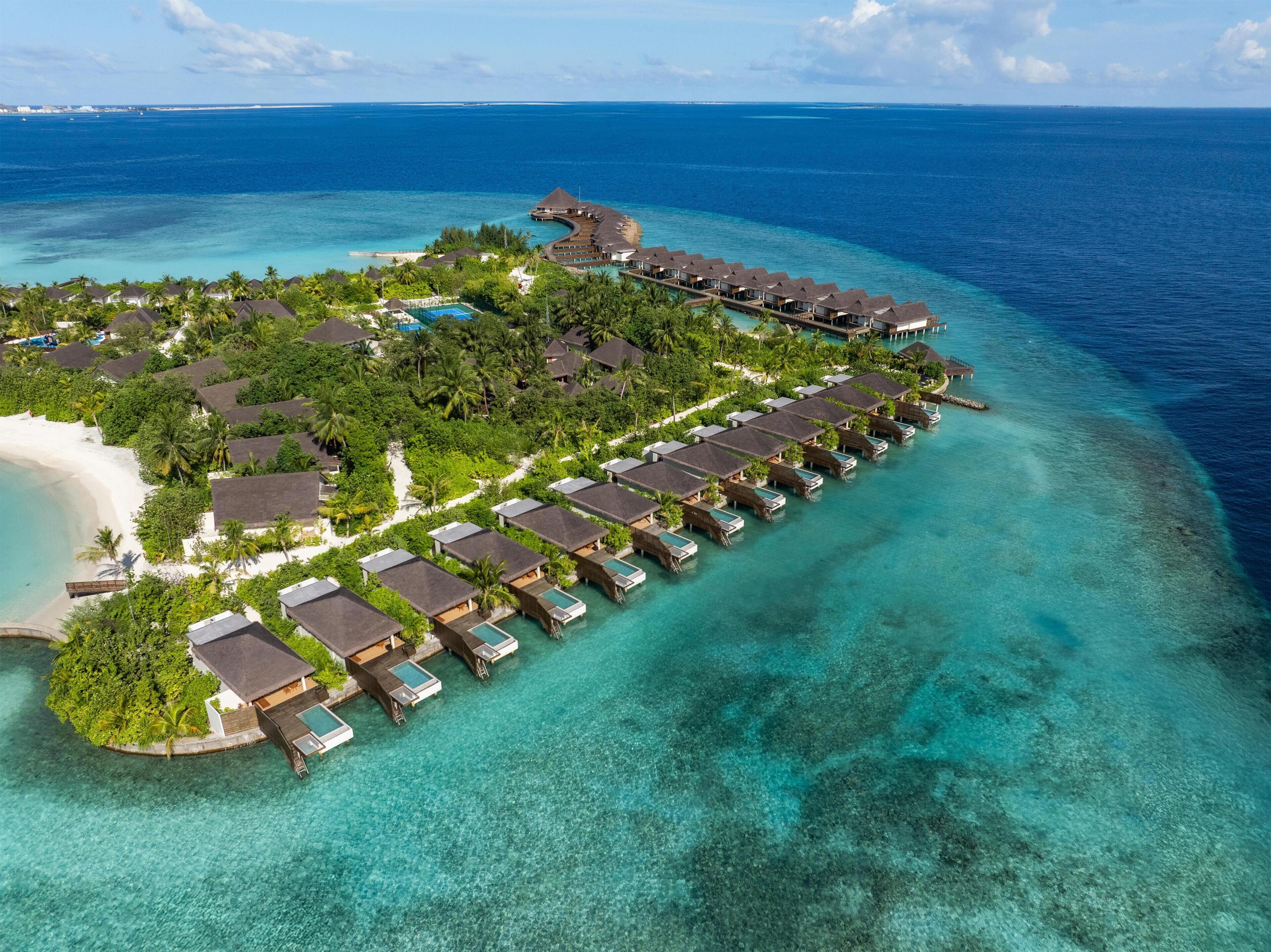 Un resort sobre el agua con alojamientos tipo bungaló, una playa y aguas turquesas cristalinas.