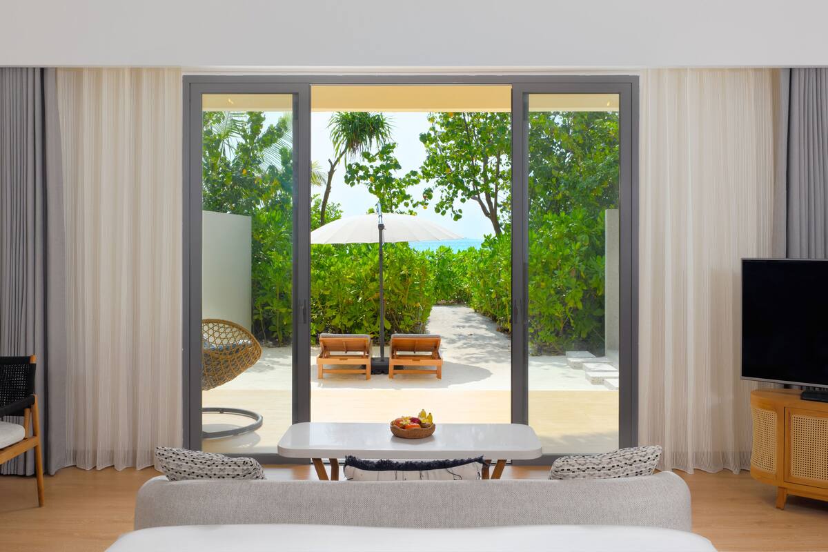 Une chambre d’hôtel moderne dotée d’une grande porte-fenêtre coulissante donnant sur un espace extérieur privatif avec une piscine, des sièges et une végétation luxuriante.