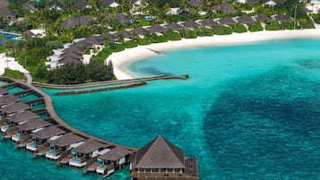 Vista aérea de um resort com bangalôs sobre a água, uma praia e águas turquesa cristalinas.