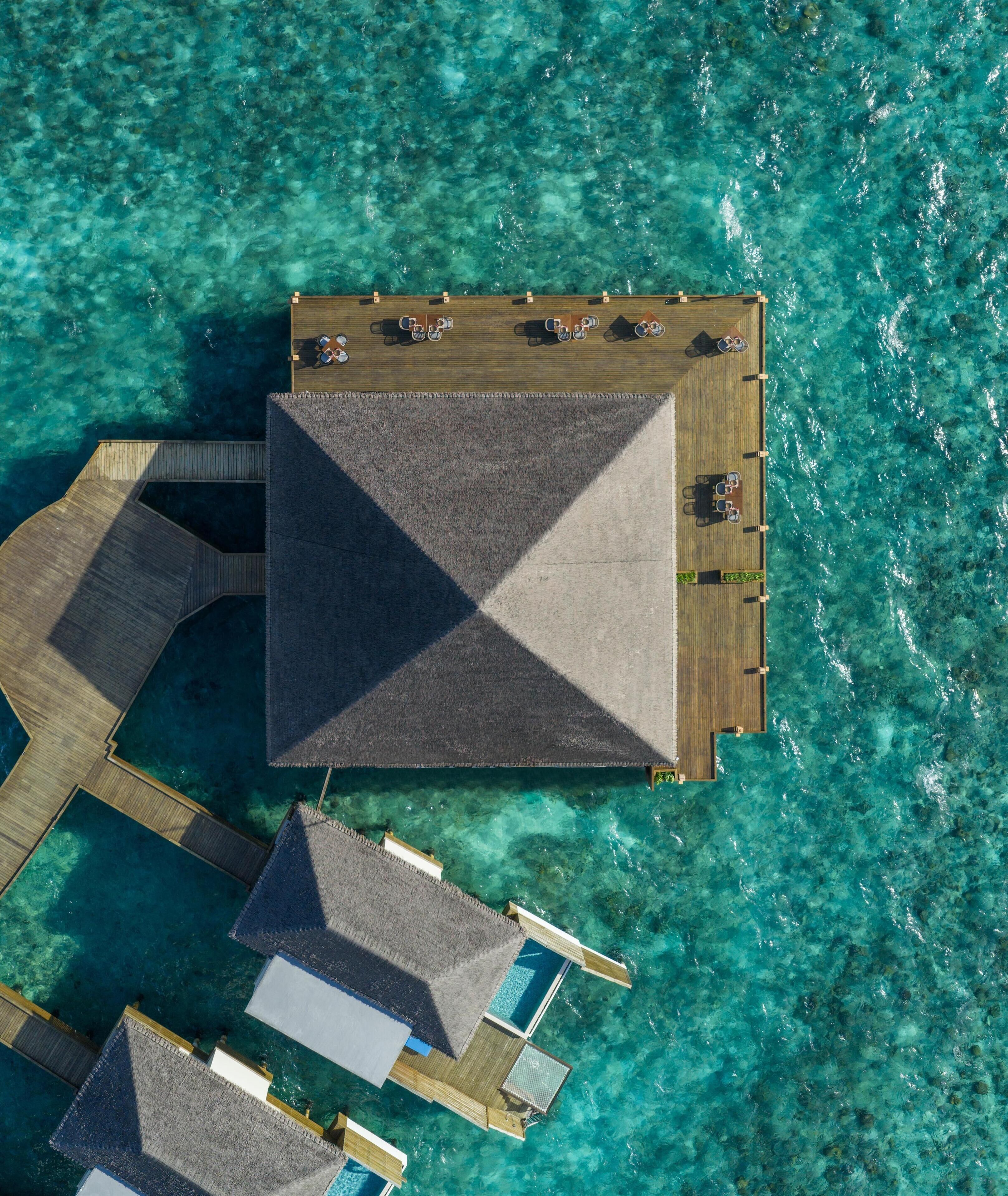 An aerial view of a resort with a large central building, multiple smaller structures, and clear turquoise waters.
