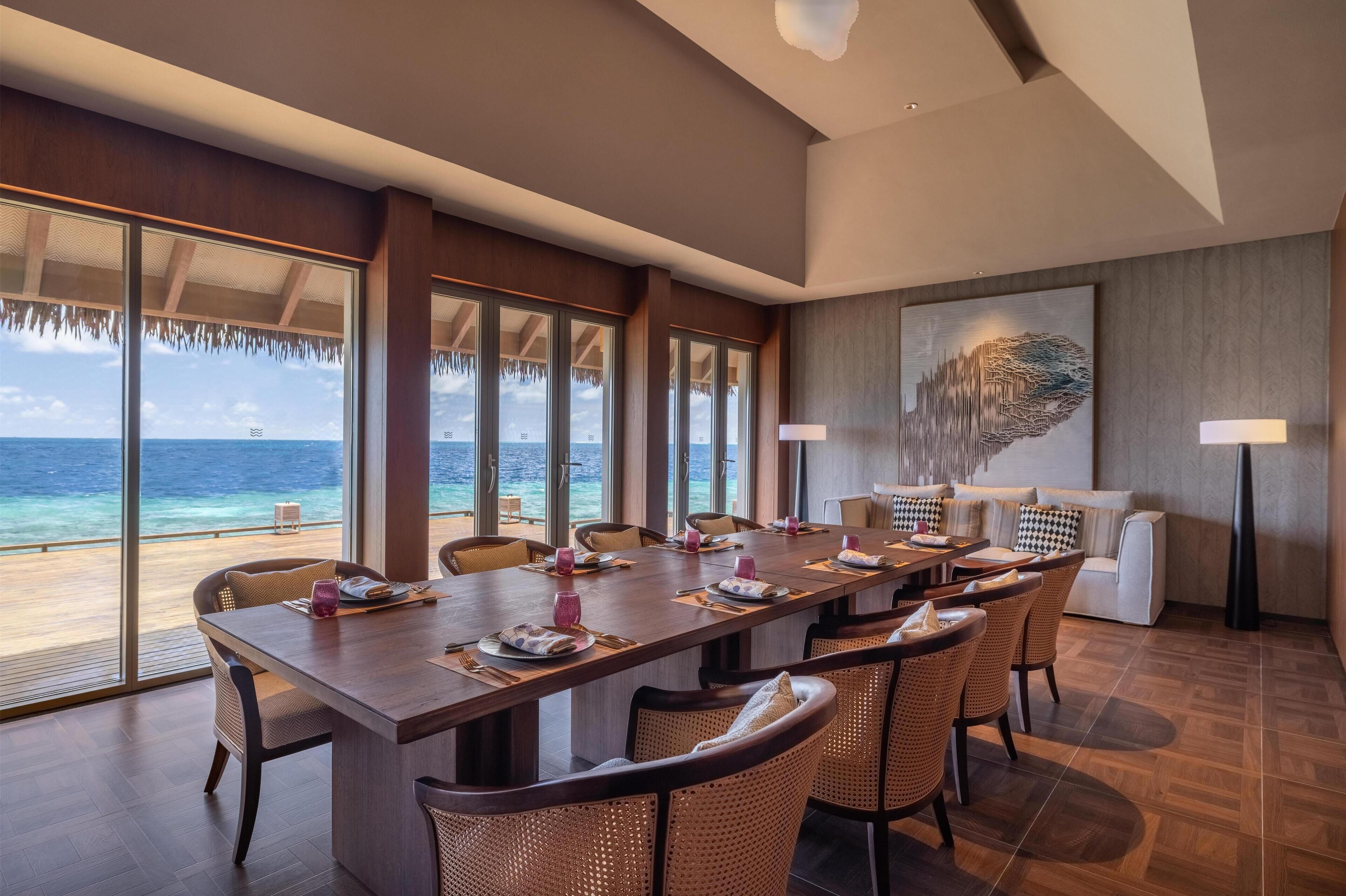 Un'ampia sala da pranzo con un tavolo lungo, sedie in vimini e vista sull'oceano.