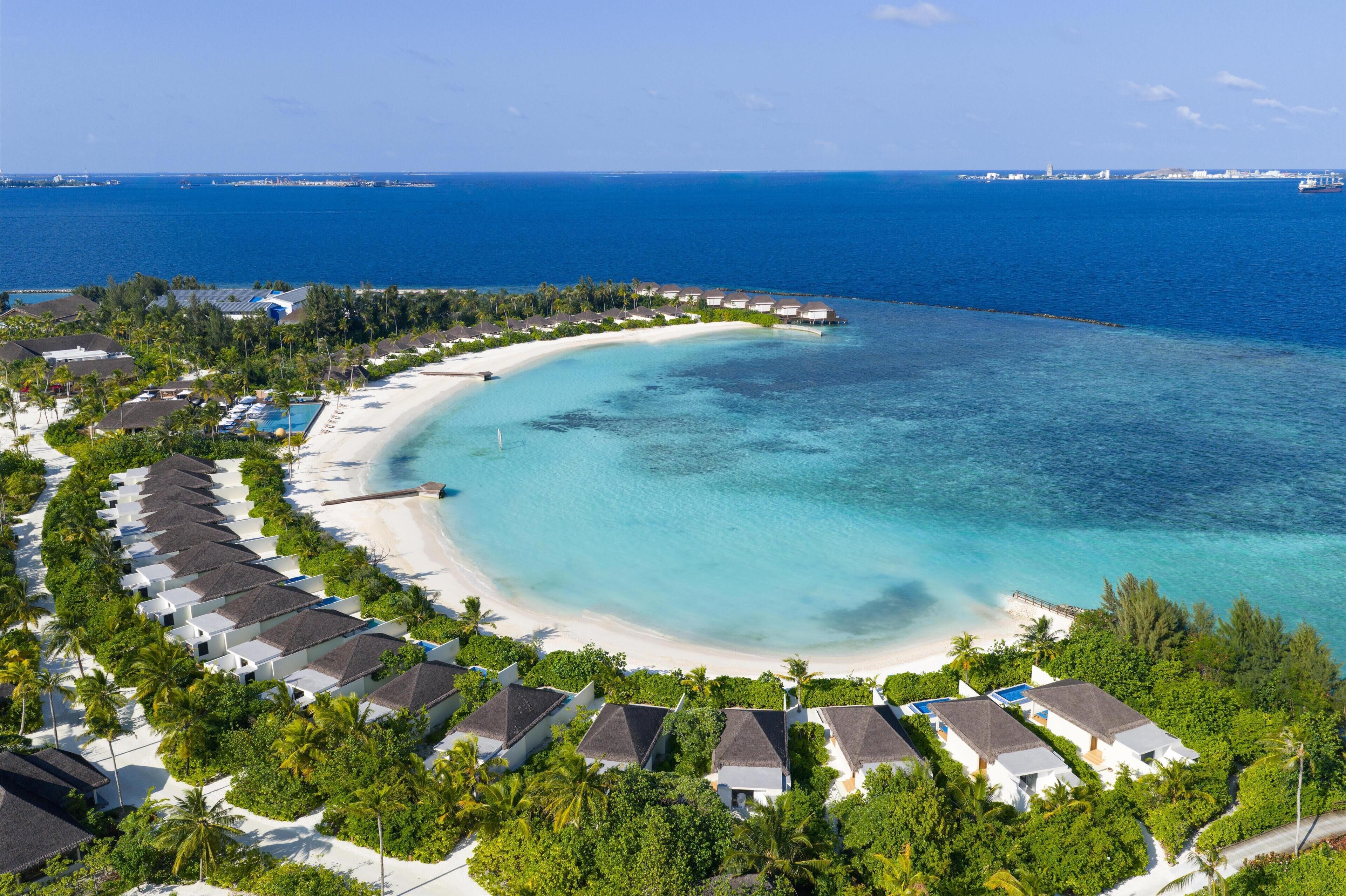 Ein Luftbild zeigt ein Resort mit Strandvillen, einem Sandstrand und klarem, blauem Wasser.
