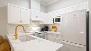A kitchen with white cabinets, a white refrigerator, a stove, and a microwave. - Luxe Studio - 102A (Kelowna)