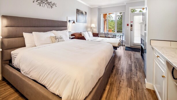 A modern bedroom with a large bed, bedside tables, a desk, and a view of the outdoors. - Golf Course Walk Up - 102B (Kelowna)