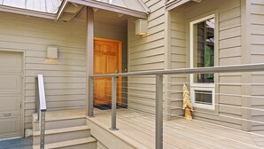 A residential building with a wooden front door, a covered porch with a metal railing, and a window with a view of the interior. - 4 Umpqua - Sunny Sunriver! Hot Tub, AC, SHARC, Amazing Location! (Bend)
