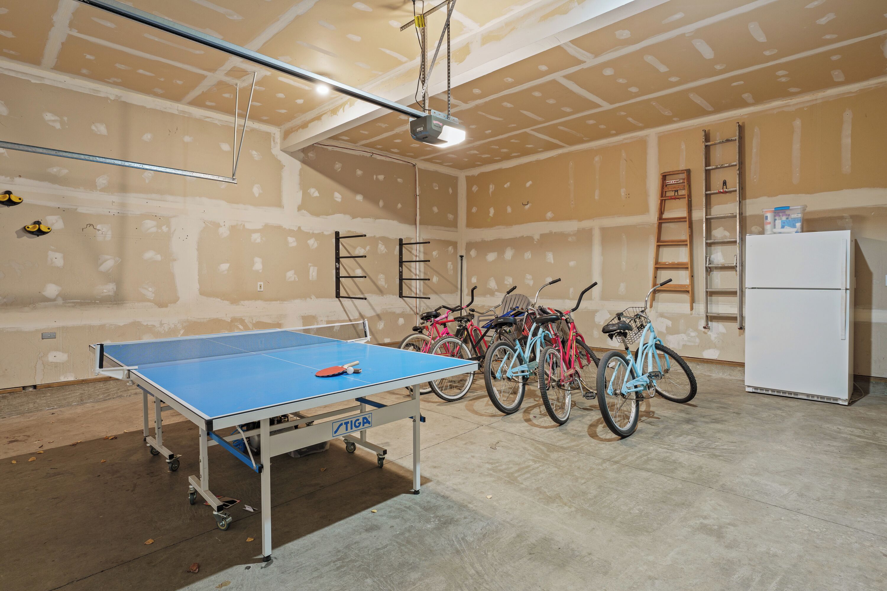 Una habitación con mesa de ping pong, bicicletas y refrigerador.