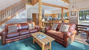 A spacious living area with a high ceiling, wooden staircase, and a kitchen in the background. - 4 Umpqua - Sunny Sunriver! Hot Tub, AC, SHARC, Amazing Location! (Bend)