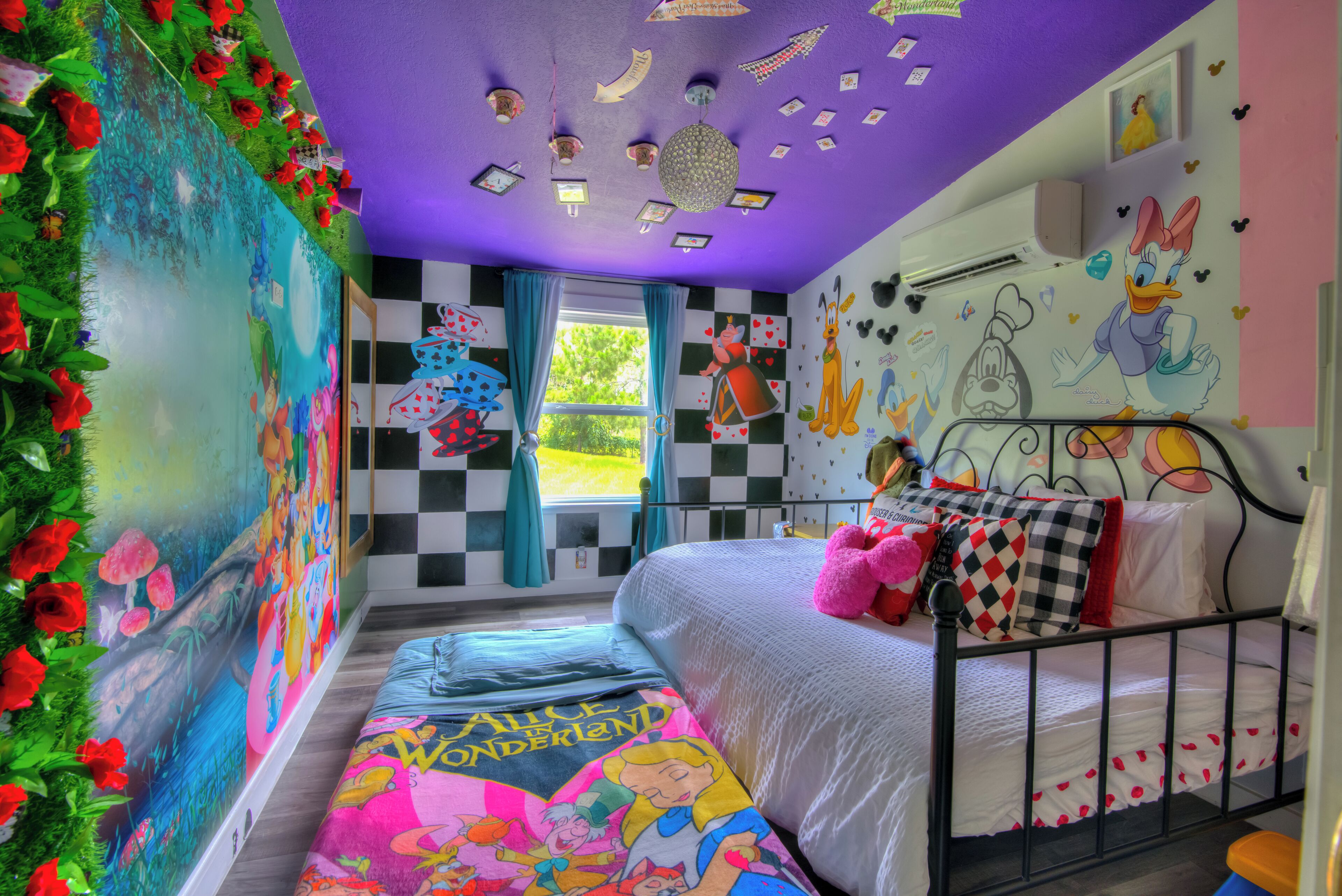 Un dormitorio con piso a cuadros, una cama con colcha temática de Disney y un mural de personajes de Disney en la pared.