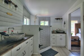 Une salle de bain dotée d’un grand lavabo sur pied, d’un meuble-lavabo en bois et d’une douche avec une porte en verre.
