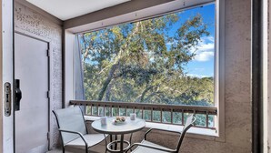 A balcony with a table and chairs, a door, and a view of trees and sky. - 889 Ketch Court @ Harbour Town, Sea Pines | Pool Access | Walk to Marina & Golf Links (Hilton Head Island)
