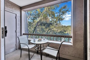 Ein Balkon mit Tisch, Stühlen, einer Tür und Blick auf Bäume und Himmel.
