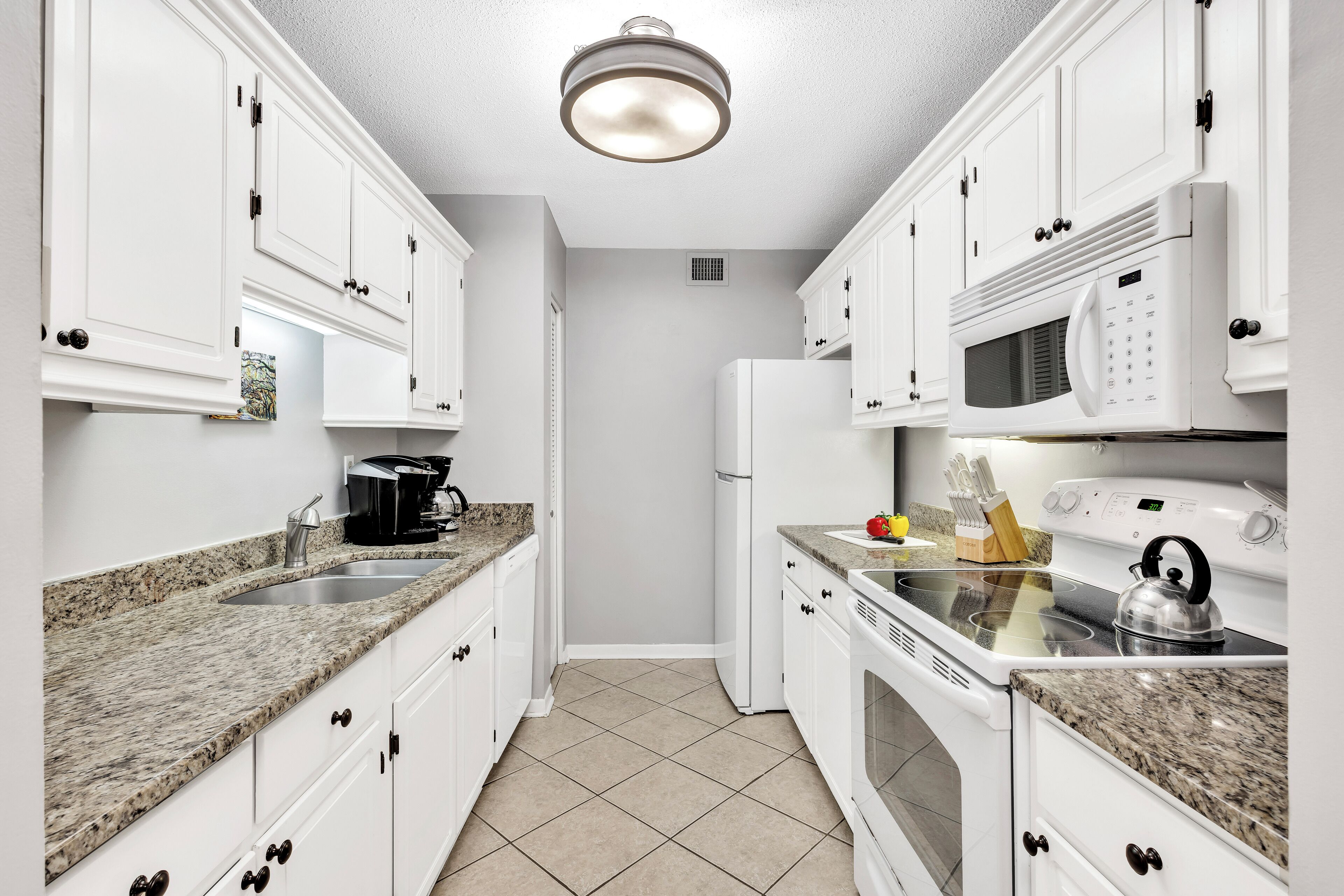 A modern kitchen with white cabinets, granite countertops, a built-in microwave, and a stove.