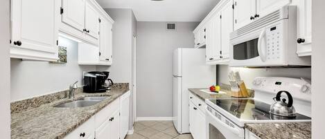A modern kitchen with white cabinets, granite countertops, a built-in microwave, and a stove.