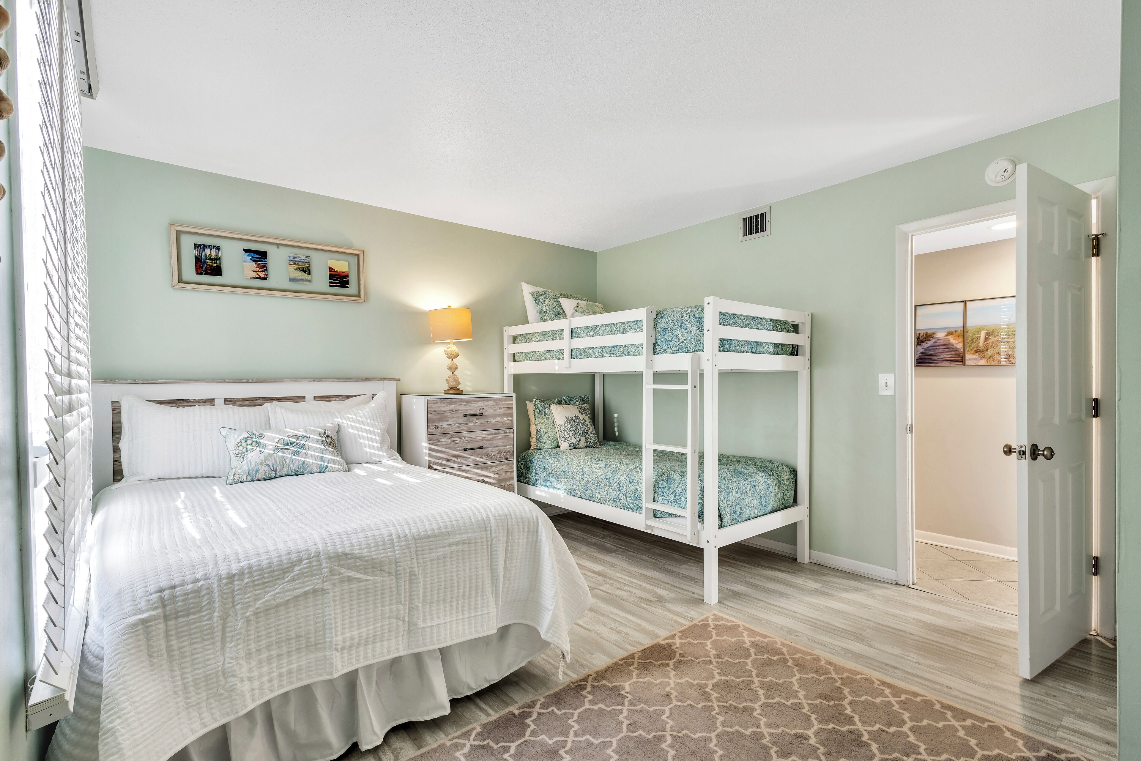 A bedroom with a bunk bed, a single bed, a nightstand, a lamp, and a framed picture on the wall.