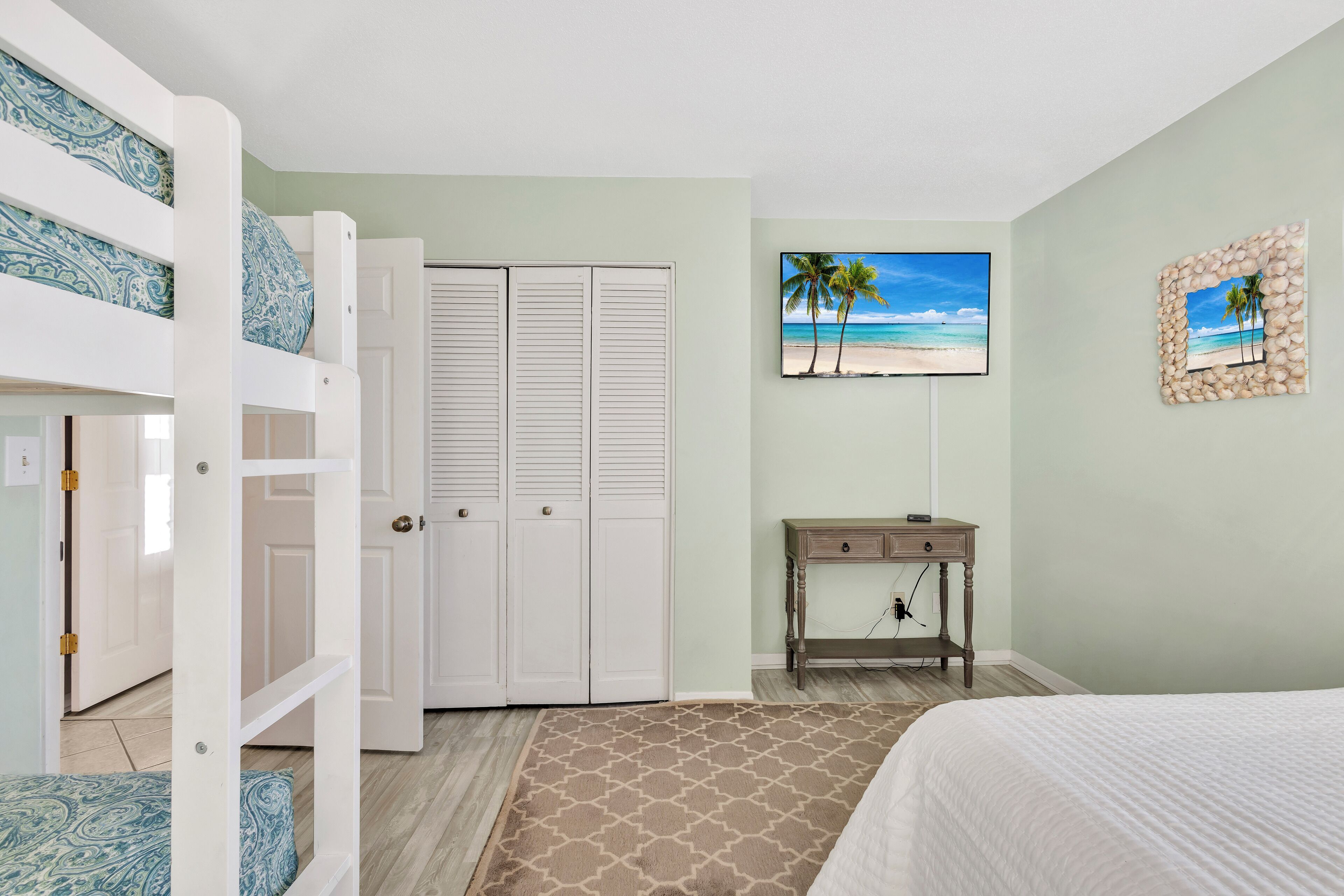 Une chambre avec des lits superposés, un bureau, une chaise et une décoration murale sur le thème de la plage.