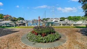 A marina with boats, a lighthouse, and a brick pathway with a flower bed. - 889 Ketch Court @ Harbour Town, Sea Pines | Pool Access | Walk to Marina & Golf Links (Hilton Head Island)