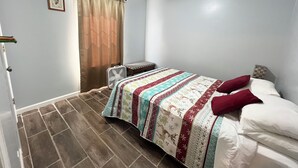 A bedroom with a bed, a bedside table, a fan, a window with curtains, and a picture on the wall.