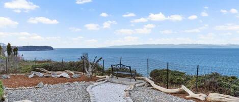 A coastal view with a pebble path, a bench, and a fence overlooking the sea.